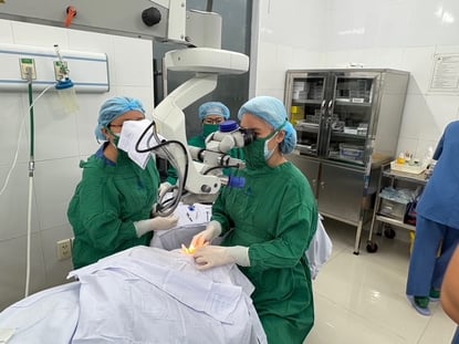 Two medical professionals look through a medical device while performing a medical procedure.