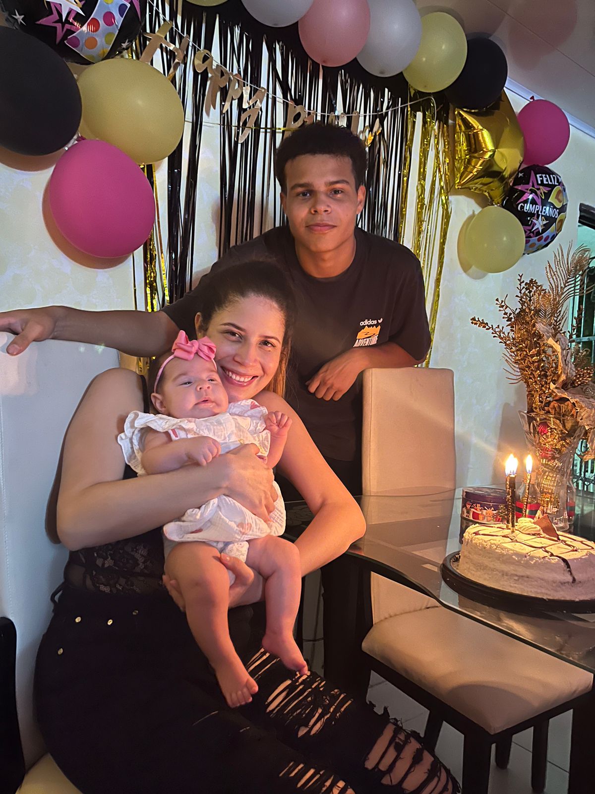 Santiago Villalobos standing behind a woman holding a baby at a birthday party.